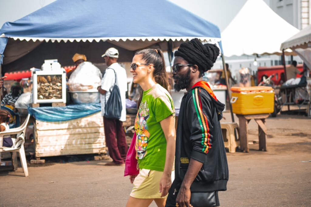About Us A cheerful couple enjoys a walk through a bustling market in Accra, Ghana, capturing local life and culture.
