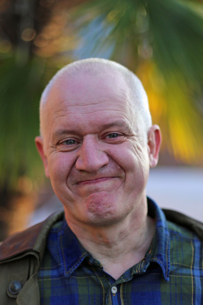 Home Portrait of a smiling bald man outdoors with palm tree in background, radiating happiness and warmth.