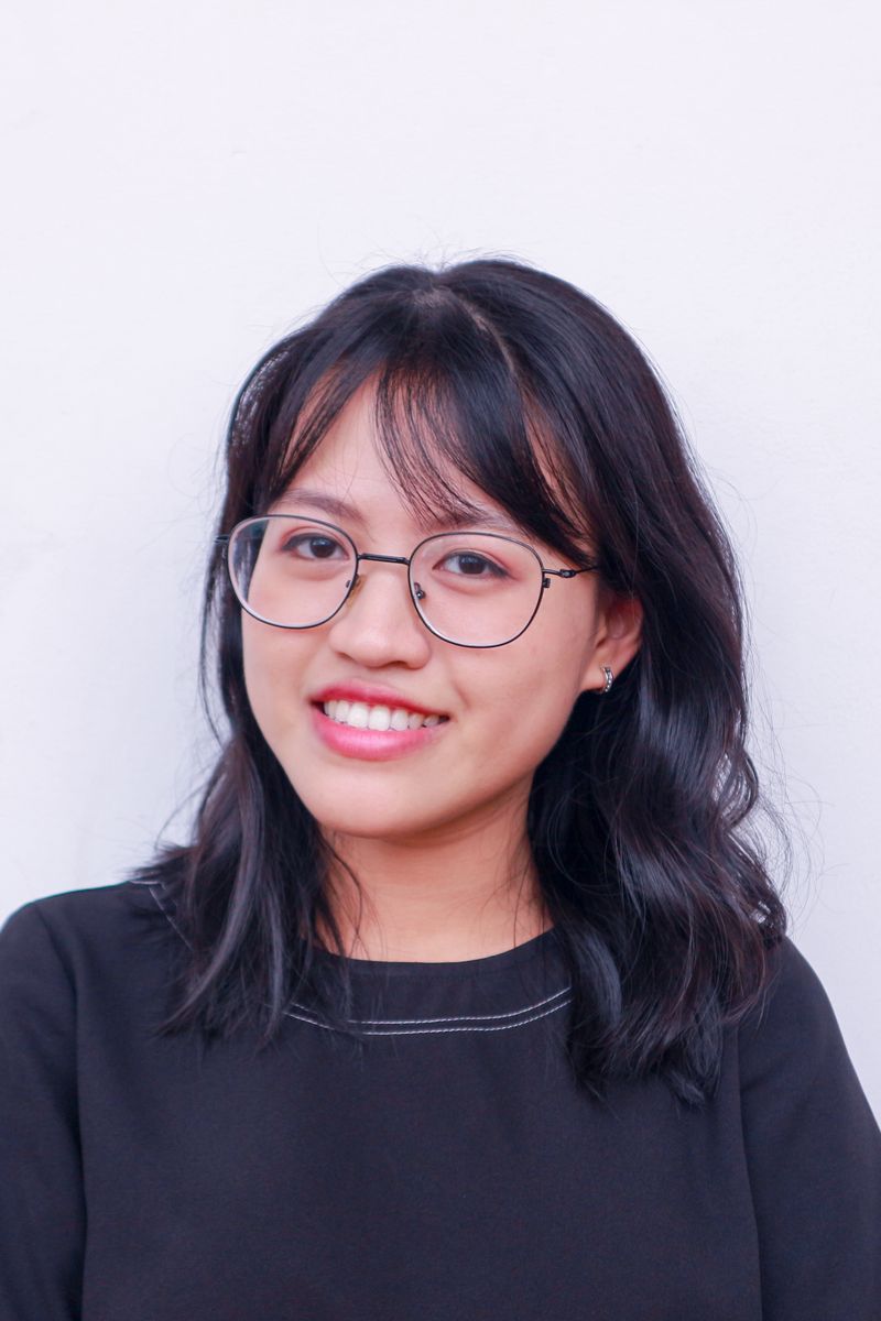 Home Portrait of a young woman with glasses and black hair smiling against a plain background.