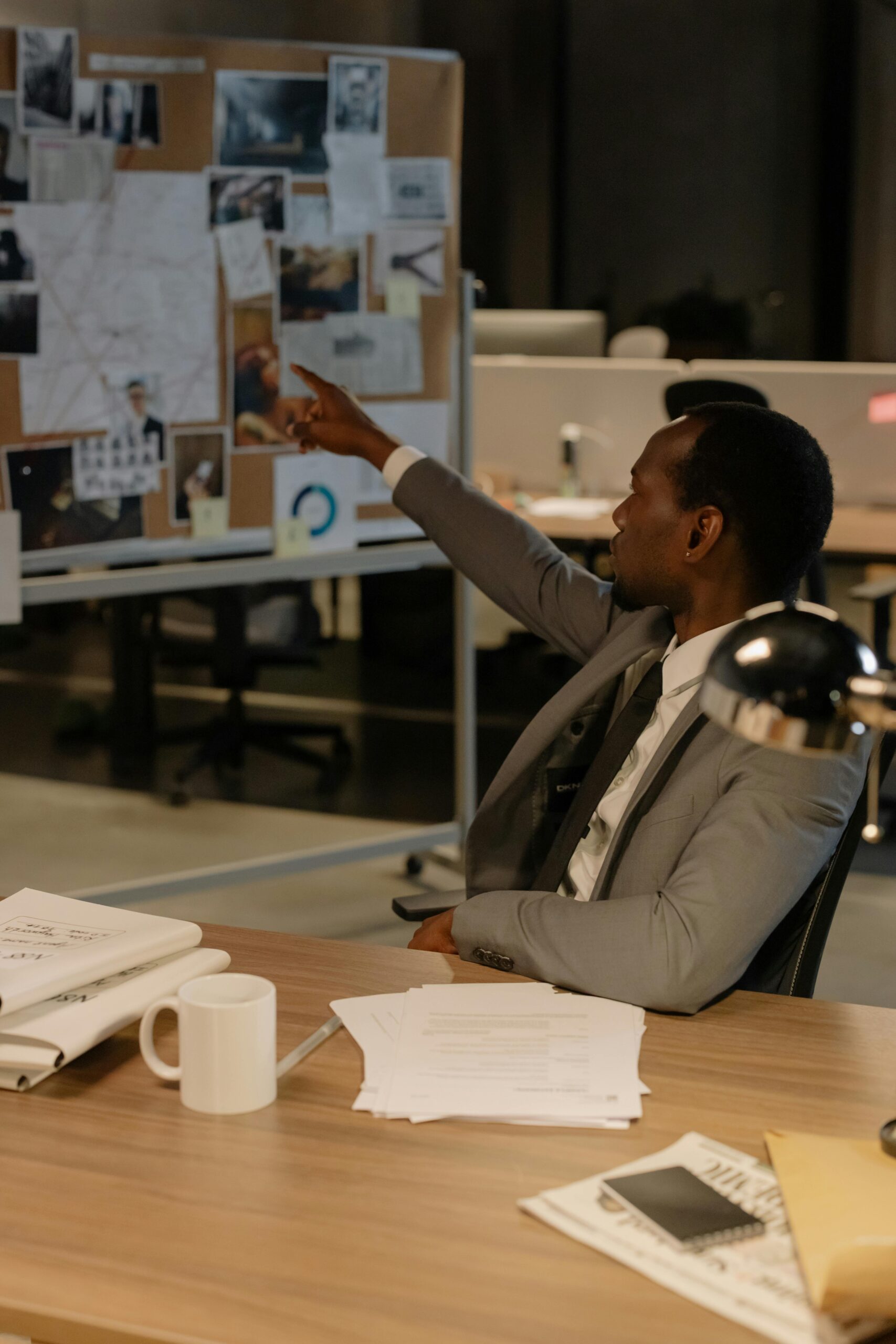 Home An African man in a suit points at a board full of evidence in an office setting.